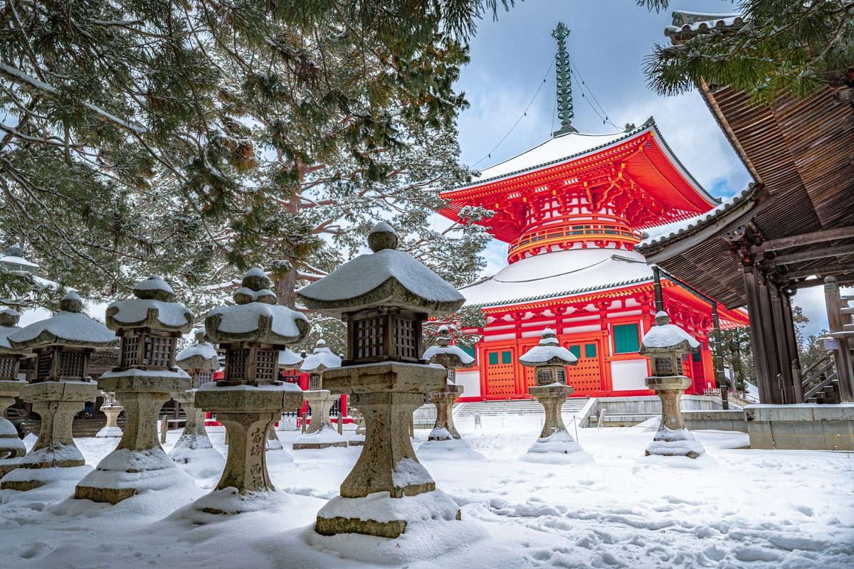 Un tempio giapponese vermiglio nella neve, con le lanterne di pietra imbiancate in primo piano
