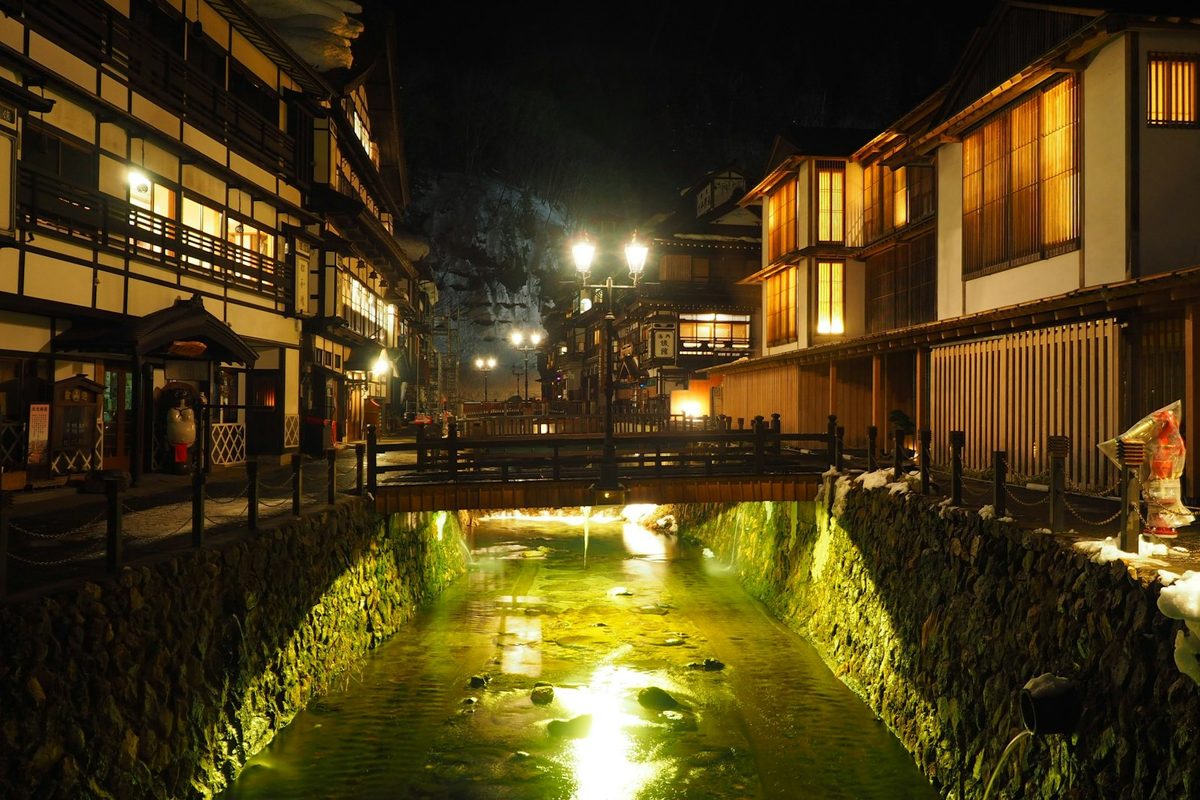 Le locande di legno illuminate di Ginzan Onsen lungo il torrente, con la neve sui bordi