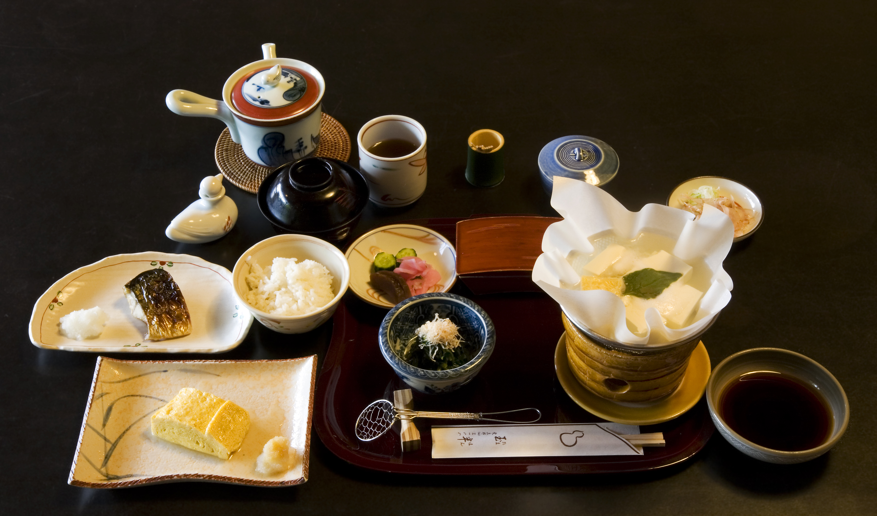 Un kaiseki con ciotole laccate rosse e nere disposte con cura su un vassoio di legno, simbolo dell'eleganza della cucina giapponese tradizionale