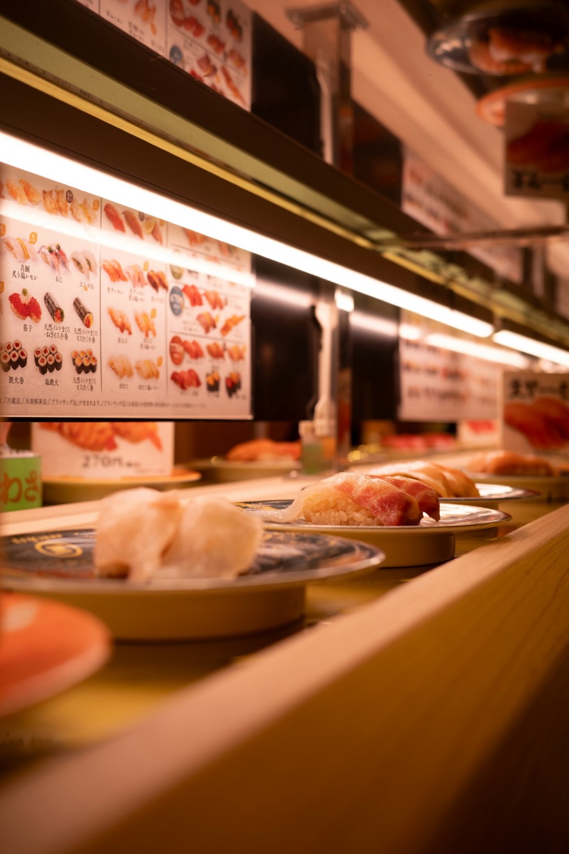 Il nastro trasportatore di un kaiten sushi giapponese con piattini di nigiri e i cartelli del menù in giapponese