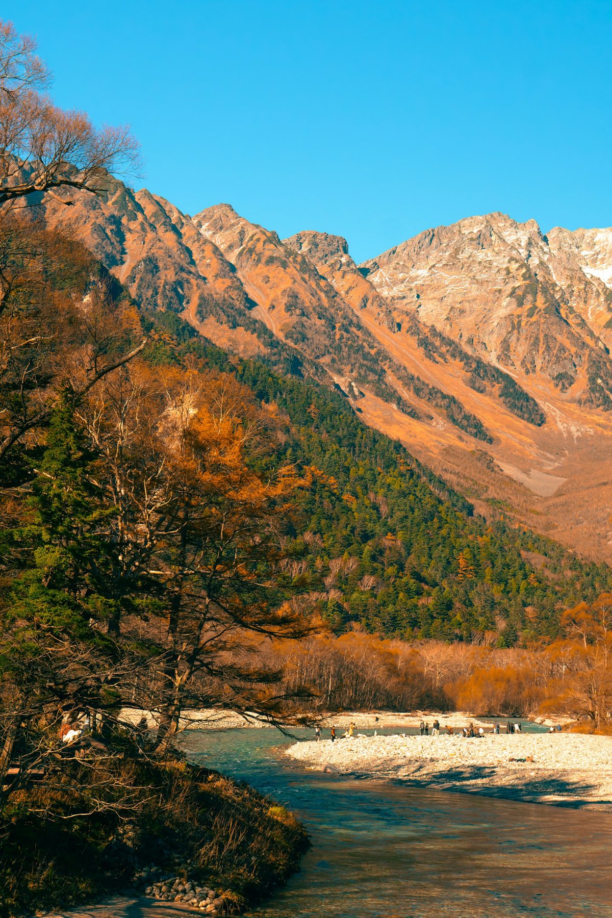 Kamikochi in autunno, con il foliage rosso e dorato lungo il fiume e le montagne alle spalle