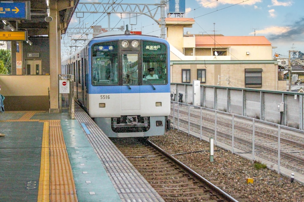 Un treno locale bianco e blu diretto verso Kobe fermo in stazione, con i cartelli in giapponese per Himeji e l'uscita