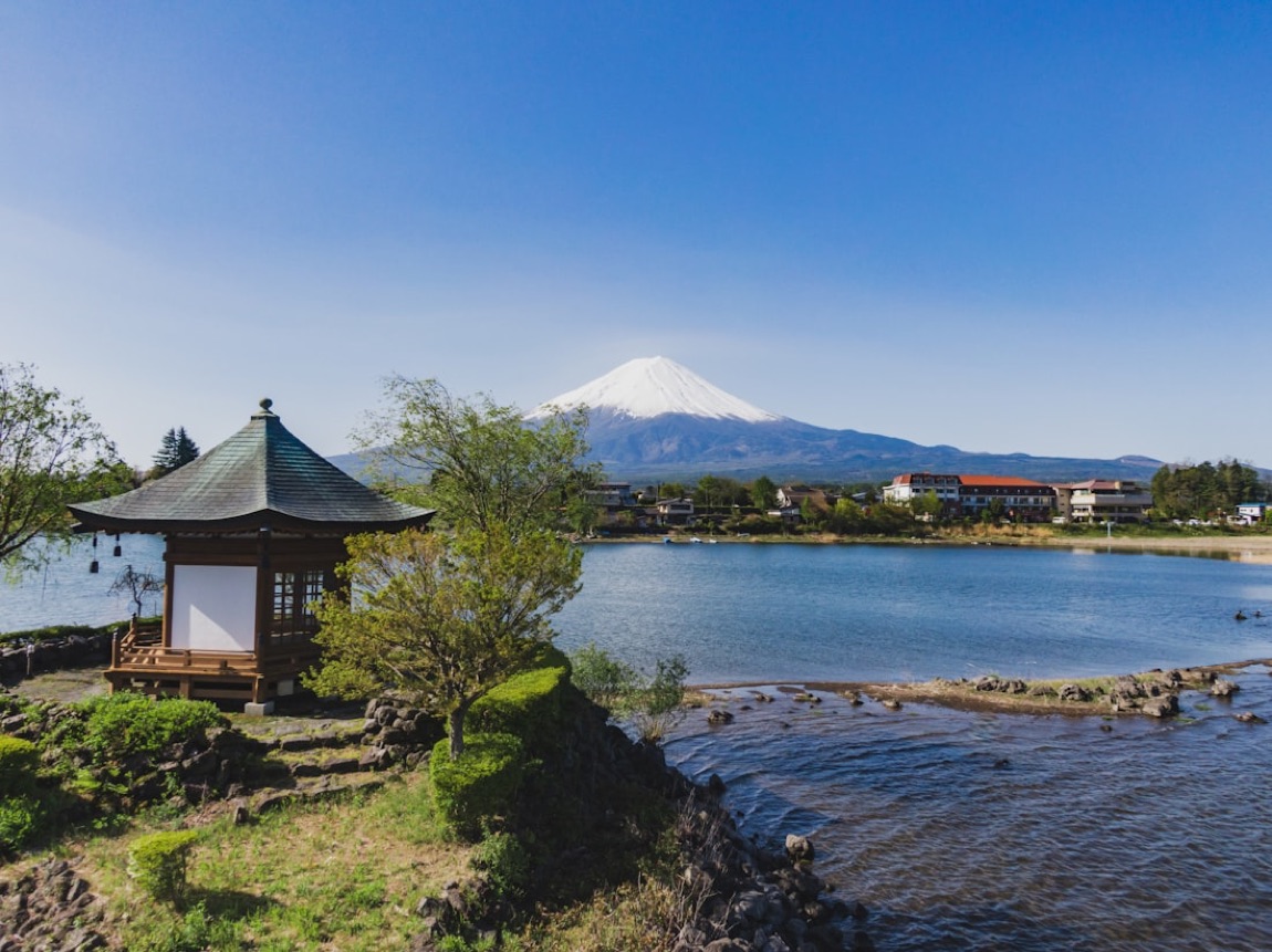 Il lago Kawaguchi con un padiglione giapponese in riva e il Monte Fuji innevato sullo sfondo, sotto un cielo azzurro