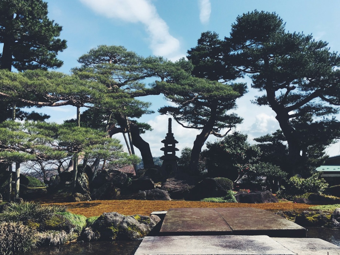 Il giardino Kenrokuen di Kanazawa con una lanterna di pietra tra i pini sotto un cielo azzurro