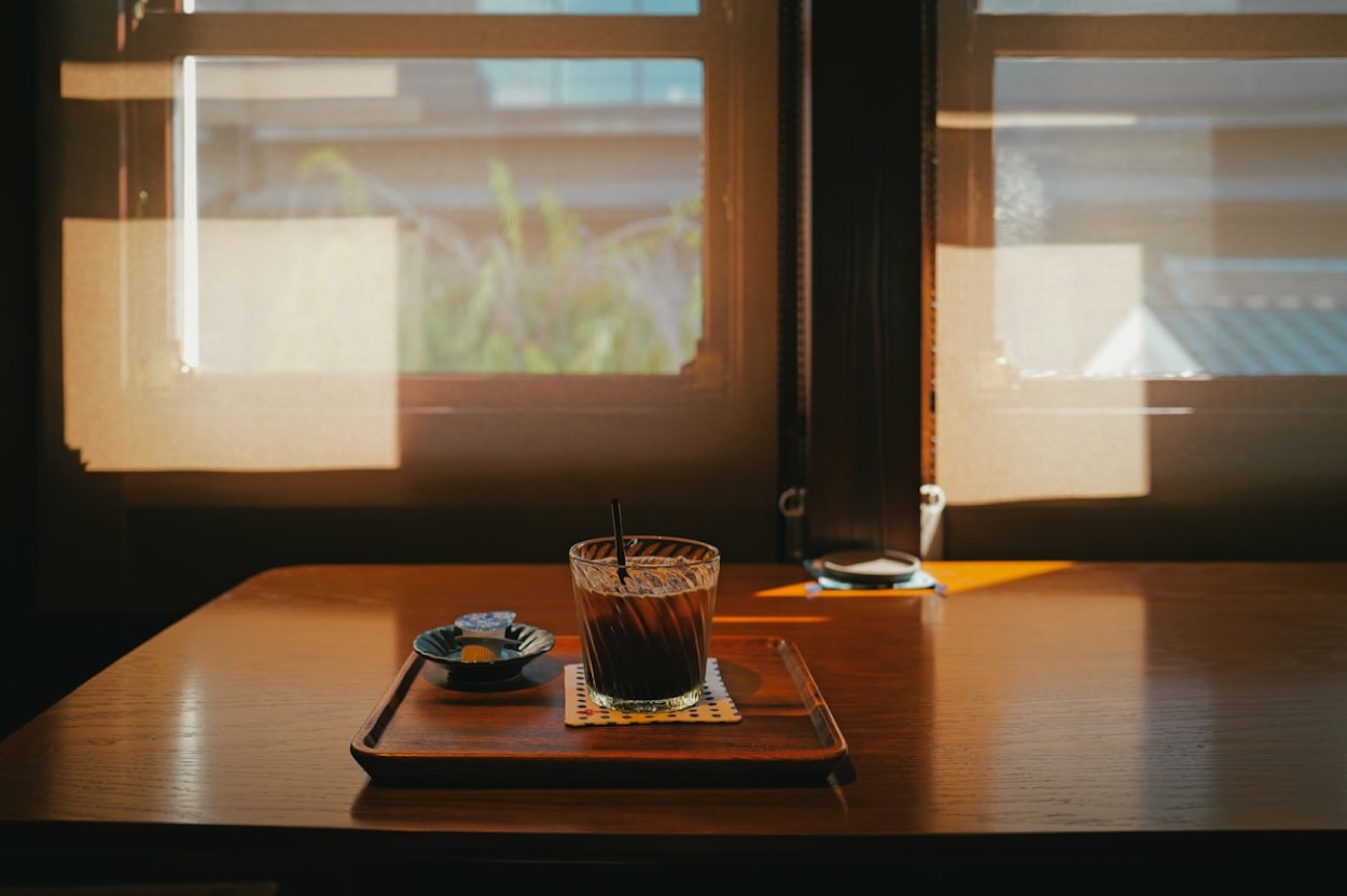 L'interno di un caffè giapponese retrò: un caffè freddo su un vassoio di legno accanto a una finestra, nella luce calma del pomeriggio