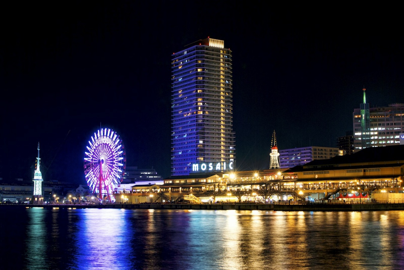 Il lungomare di Harborland a Kobe di notte, con la ruota panoramica illuminata e i palazzi che si riflettono nell'acqua