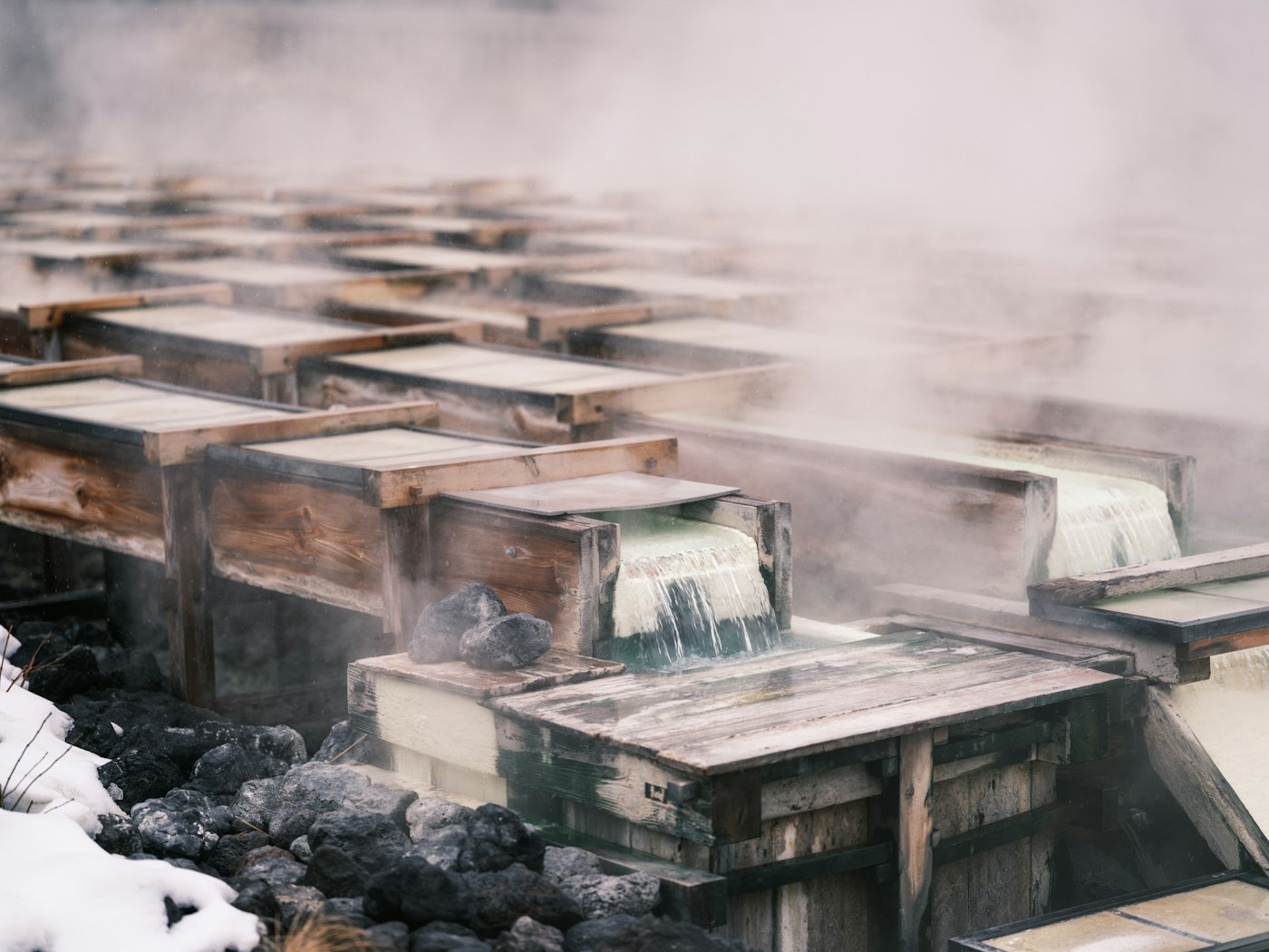 Lo Yubatake di Kusatsu: le canaline di legno da cui scorre l'acqua termale fumante, tra rocce vulcaniche coperte di neve