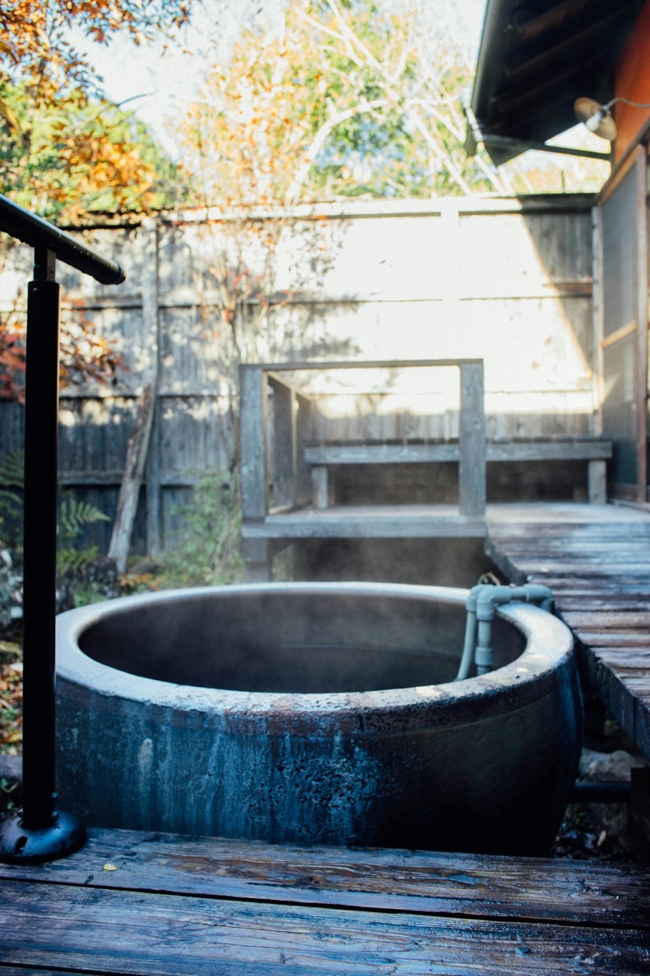 Una vasca termale privata all'aperto, in pietra, con il vapore che sale, su una veranda di legno tra gli aceri d'autunno