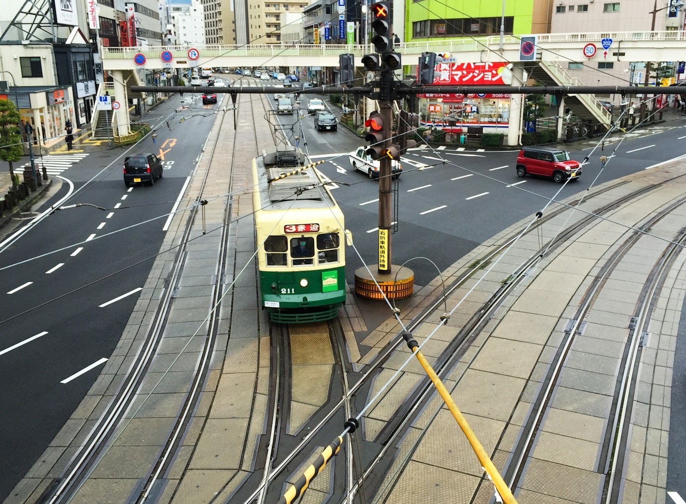 Un tram storico verde e crema di Nagasaki a un incrocio del centro, tra insegne giapponesi