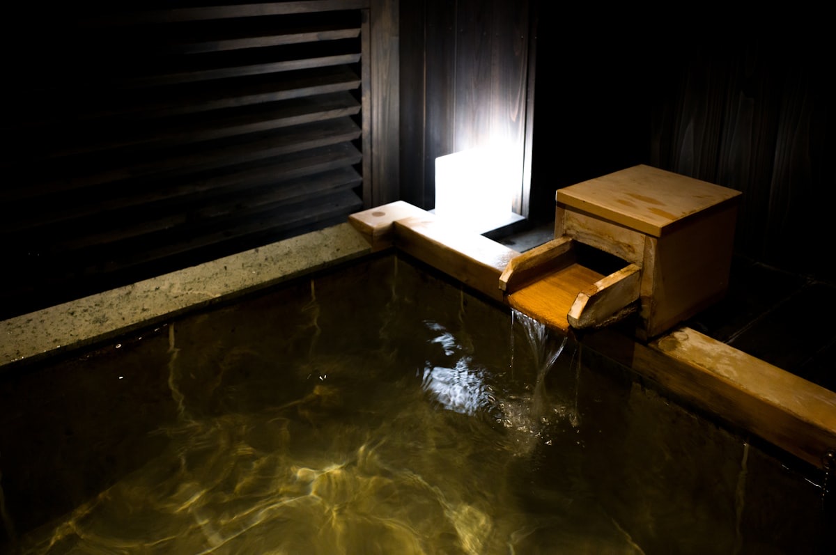 Una vasca termale in legno e pietra, con l'acqua che scorre da una bocchetta di legno