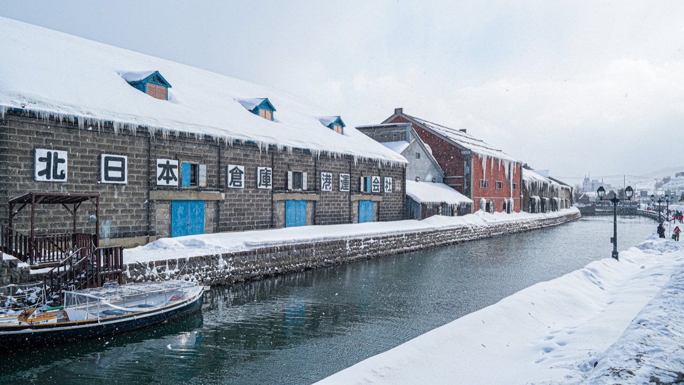 Il canale di Otaru di giorno, coperto di neve, con i magazzini di pietra e il cielo azzurro