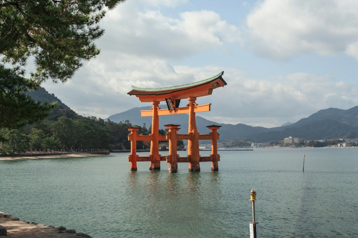 Il grande torii rosso di Miyajima che si staglia sull'acqua, con le colline verdi sullo sfondo