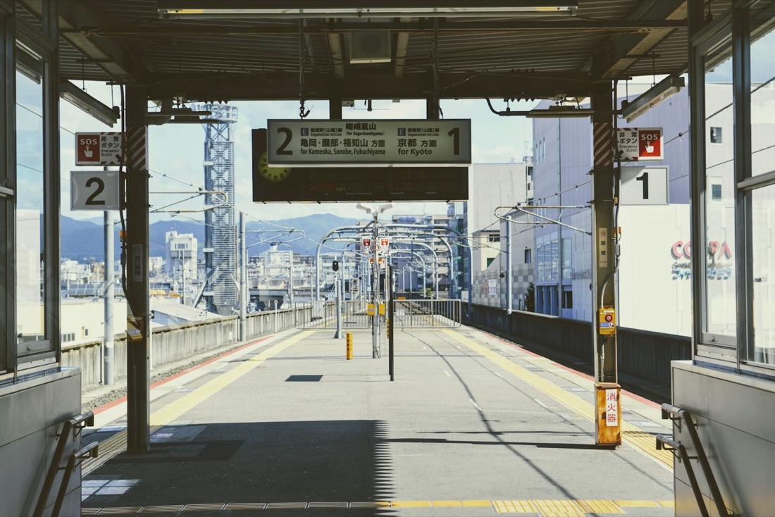 Una banchina di stazione giapponese con i cartelli delle direzioni per Kyoto, sotto un cielo sereno