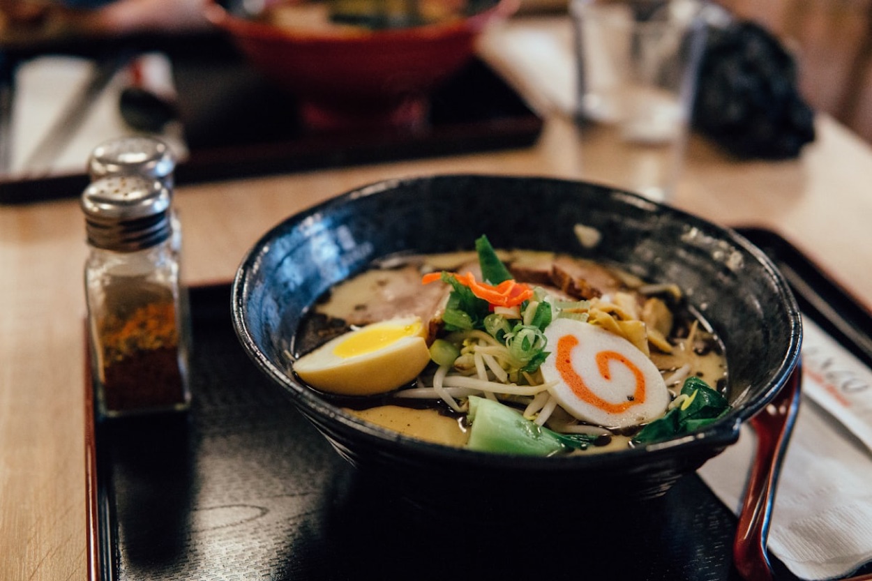Una ciotola di ramen giapponese con brodo cremoso, fettine di maiale chashu, mezzo uovo, narutomaki e verdure, su un vassoio nero