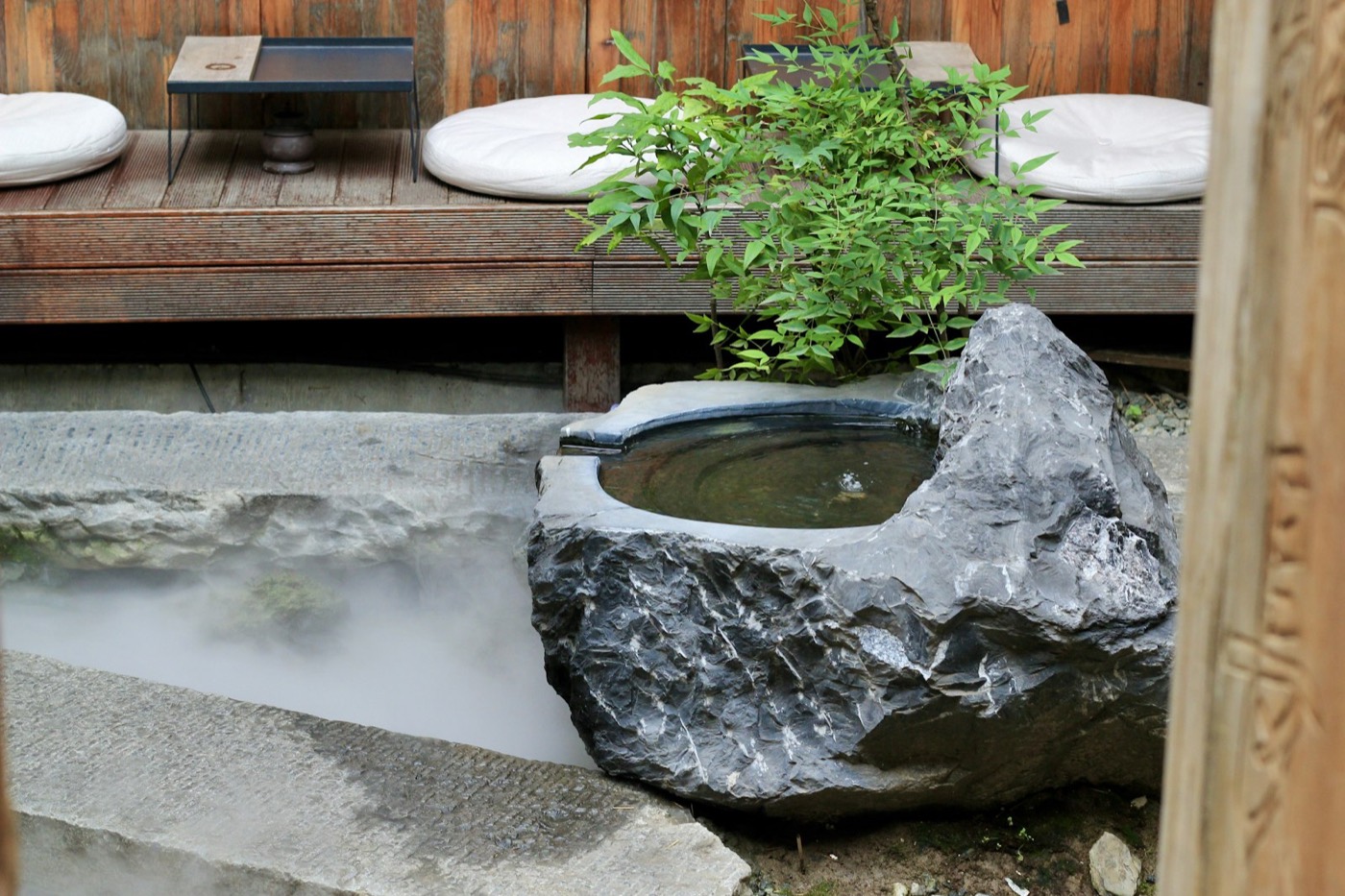 Un bagno termale all'aperto in pietra, immerso nel verde, con l'acqua che fuma nell'aria della sera