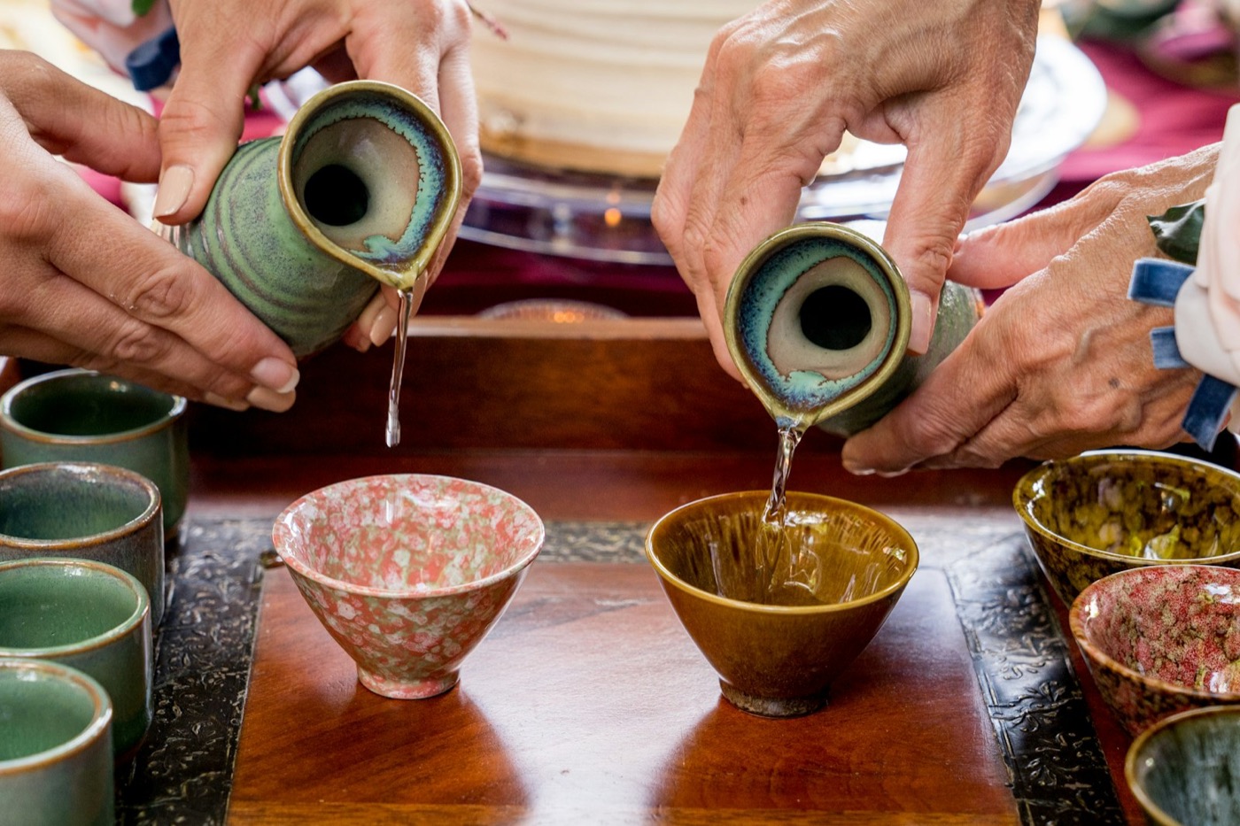 Sake versato da un tokkuri in piccole tazze di ceramica, in un servizio tradizionale