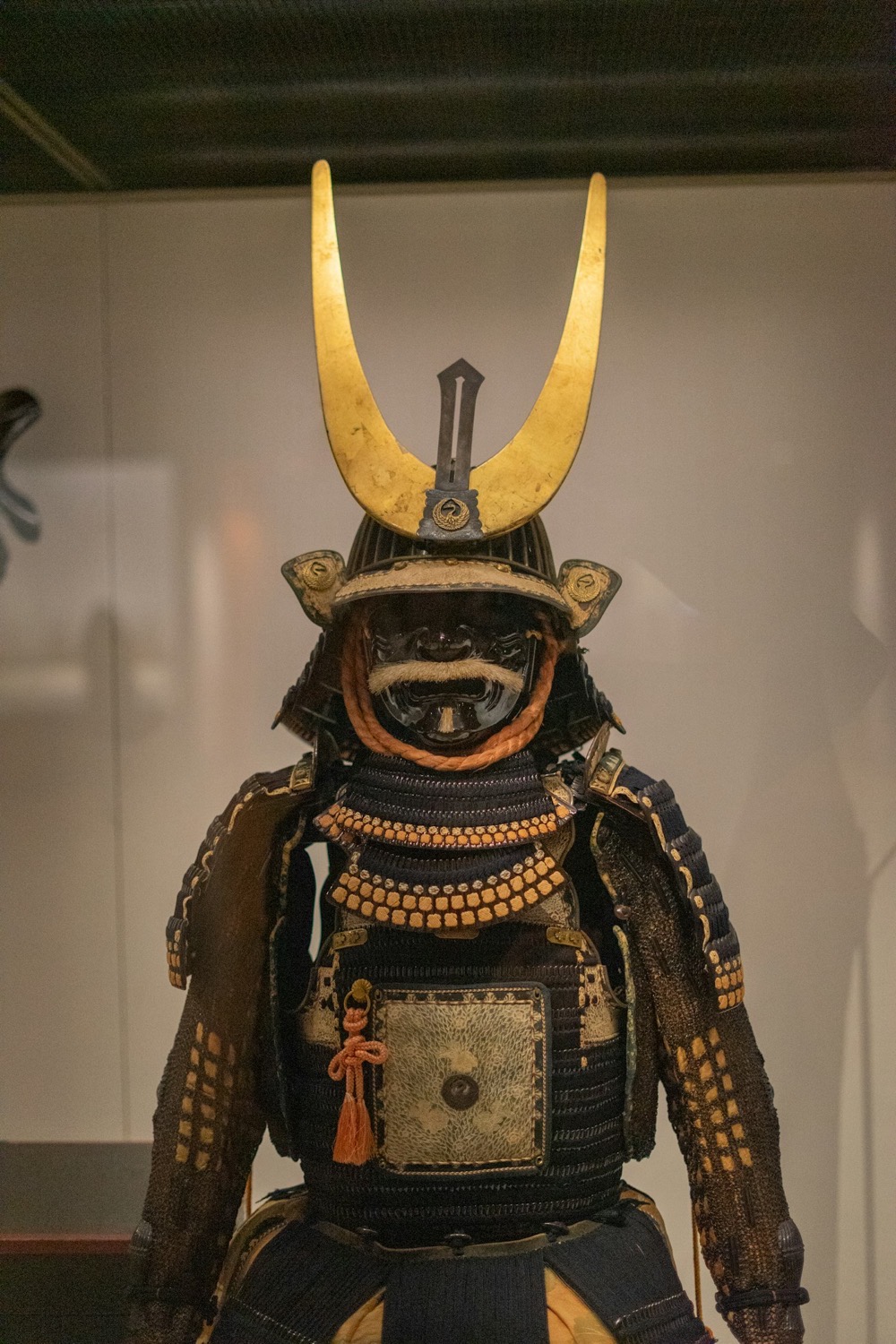 Un'armatura di samurai esposta in un museo, con l'elmo dalle grandi corna dorate e la maschera scura