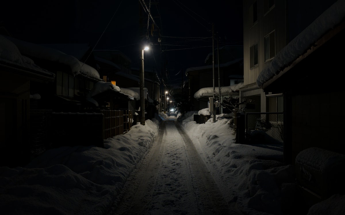 Una stradina residenziale giapponese deserta di notte, con la neve ai lati