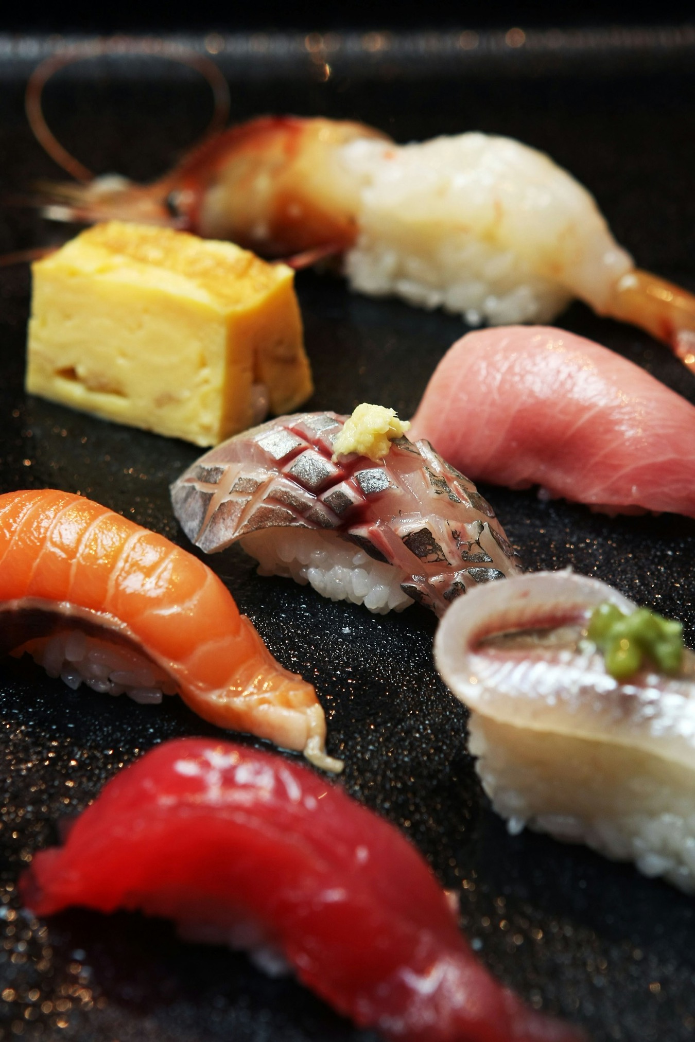 Nigiri di pregio su un piano scuro: tonno, sgombro, salmone e tamago