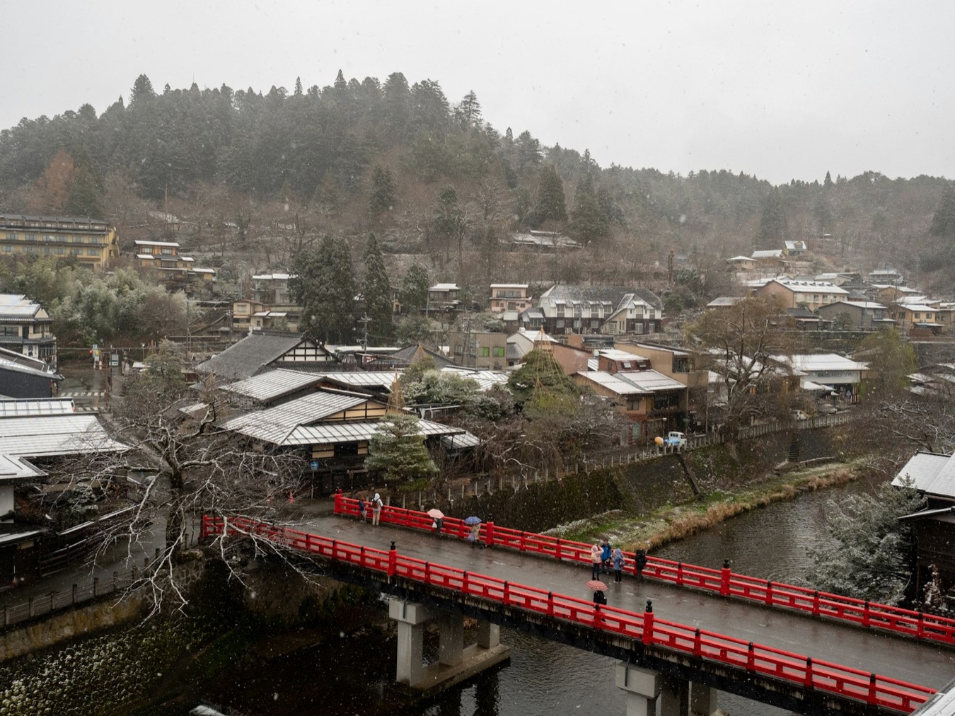 Il ponte rosso Nakabashi di Takayama sul fiume, con la neve e le montagne alle spalle