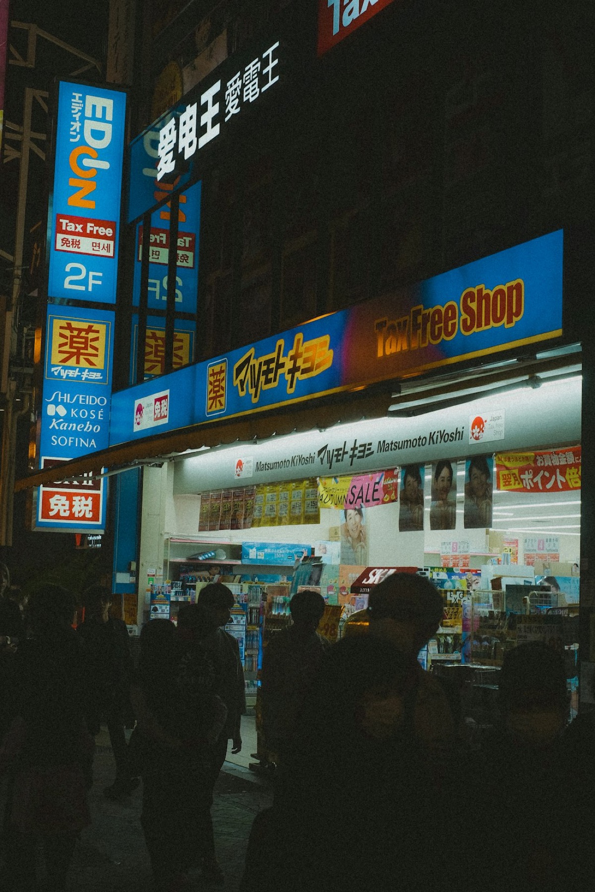 Un negozio Matsumoto Kiyoshi a Osaka di sera, con grandi insegne "Tax Free Shop" e 免税 in giapponese