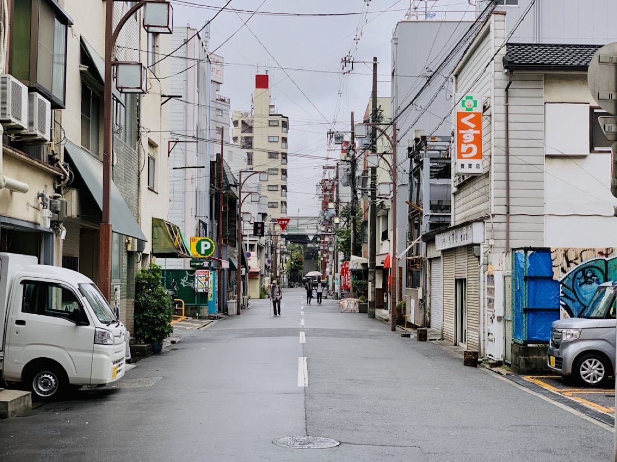Una tranquilla via di quartiere in Giappone con l'insegna di una farmacia (くすり) e un piccolo camioncino bianco