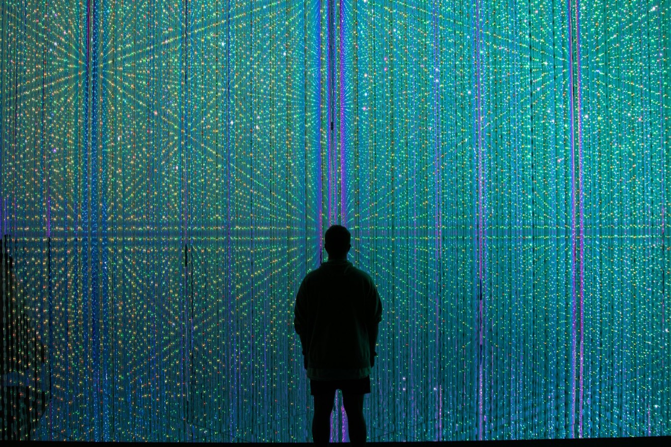 L'Universo di Cristalli di teamLab: una persona in controluce davanti a una parete di luci a LED che sembrano stelle
