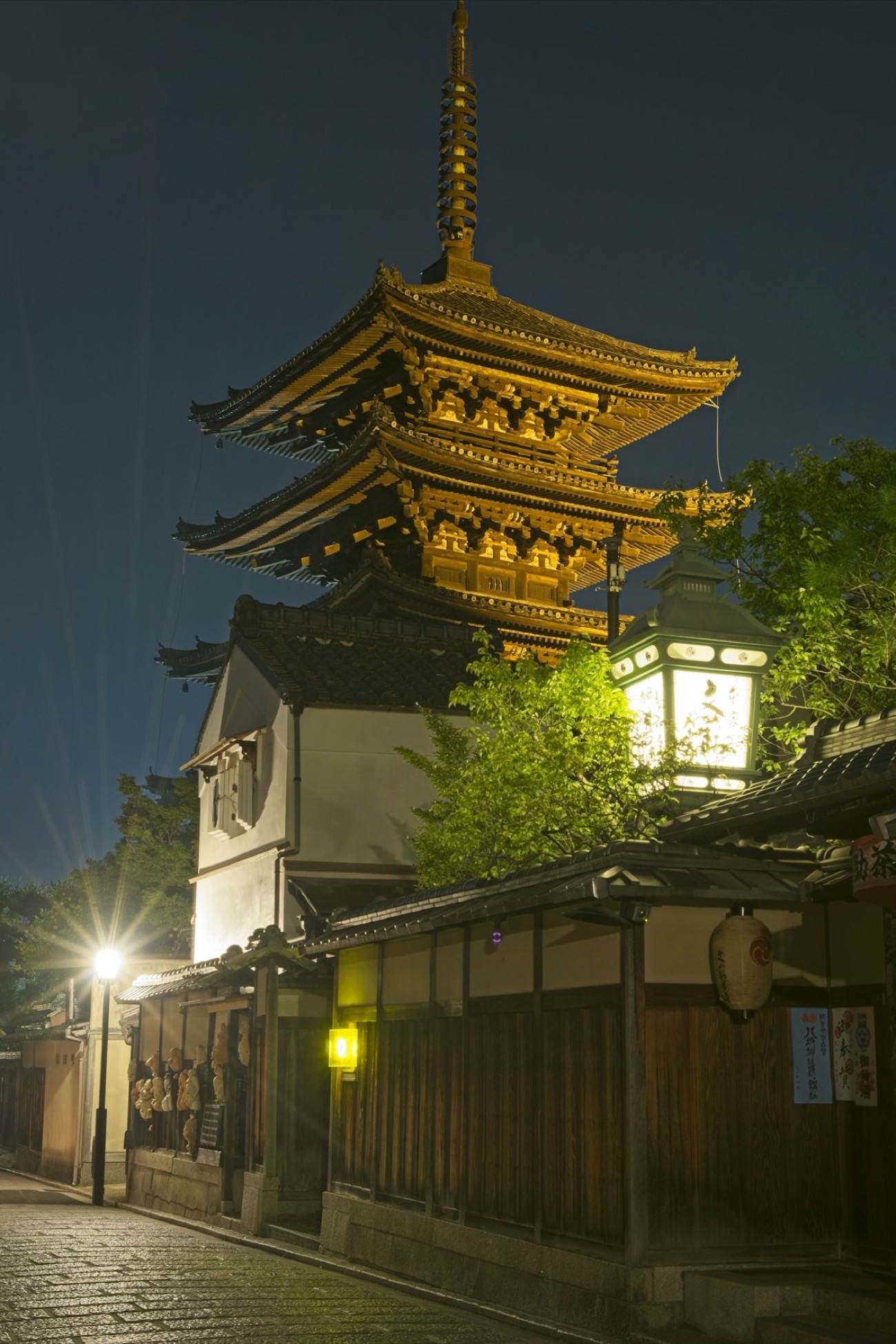 La pagoda Yasaka illuminata di notte sopra una via di case di legno di Kyoto, con una lanterna accesa