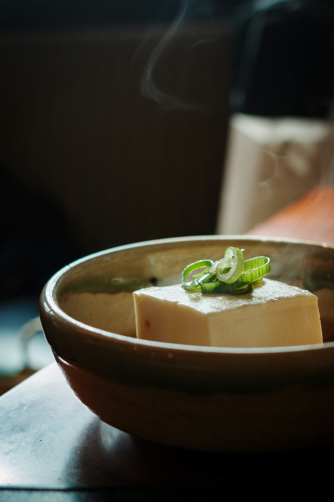 Un blocco di tofu caldo e fumante guarnito con cipollotto verde, in una ciotola di terracotta